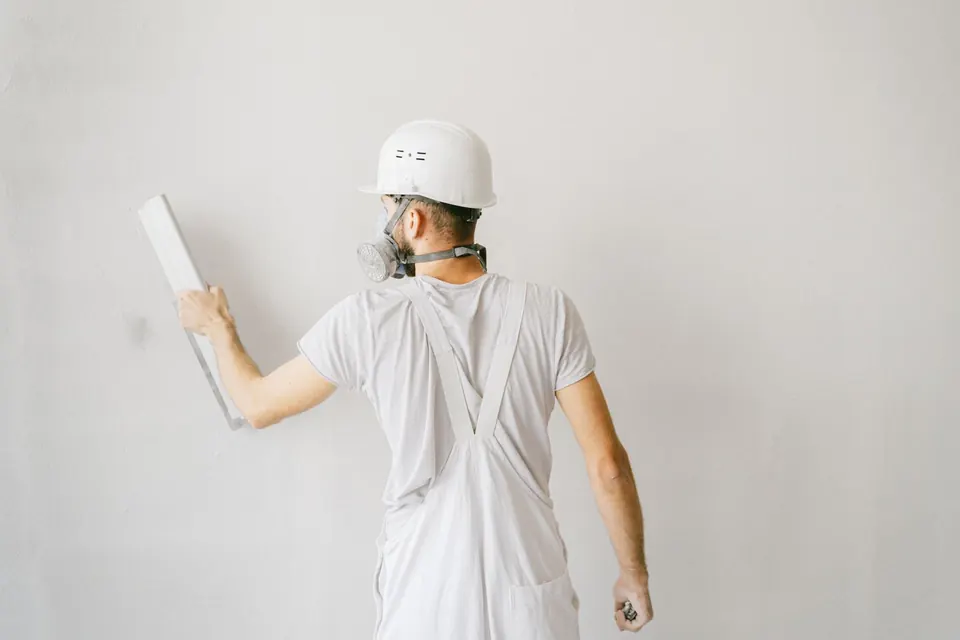Stukadoor in een witte overall trekt met een brede spaan een muur vlak, gezien van achteren